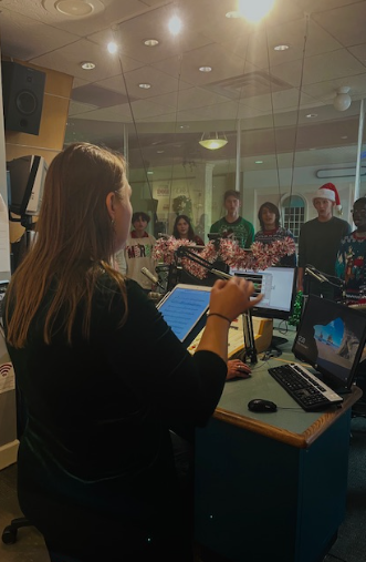 STUDIO RECORDING: Mel-High’s students sing while Ms. Natalie Taylor guides them through their songs for the recordings. The recordings were prepared for the Christmas station run by iHeartRadio. The event took place on Friday, November 7 at the station in Melbourne. Ms. Taylor worked with the station’s members to provide the students with the opportunity again. She said, “The students who were offered this opportunity are in my chamber choir which is one of our two auditioned choirs. It is a group of 16 students.”  Photo by iHeartRadio Studio Member.