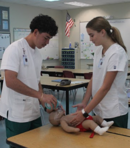 CPR training during scrub check: Gracie Ostrander and Carlito Nieves are participating in a scrub check and practicing CPR on an infant. The scrub check happened in building 9 room 900. Ostrander and Nieves wore scrubs and practiced patient care skills as part of their training. To Ostrander, hands on training is much better than lectures because “it makes you more equipped by giving you real life scenarios.” Nieves expressed “My favorite part of PCA so far is how we get to wear scrubs to school.” Photo by Ayaana Gupta