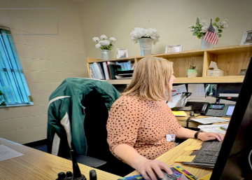 NEW STAFF SPOTLIGHT: Tammy Johnson smiles at her new desk in the front office. As the new secretary at Melbourne High School, she’s ready to take on her new responsibilities. Tammy Johnson is eager to make a positive impact in her new position. Johnson shared, “I am very excited to be in my new role as Secretary. I am going to work very hard to make the transition as smooth as possible for all.” Her enthusiasm reflects the welcoming spirit of the MHS staff. Photo by: Brooke Johnson