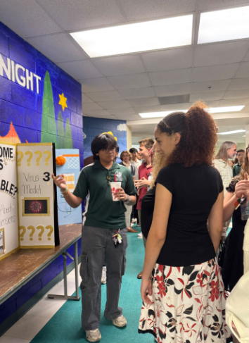 By The Board: At the IB Induction, senior Raphael Yucon presents his TOK exhibition board to incoming IB juniors. Before the official ceremony, the juniors walked through the 8 building to observe projects that they would have to do later in the year. Yucon was glad that he got to present his exhibition. “The best part [of induction] was definitely presenting my exhibition. I had forgotten how fun it was presenting to the current juniors so it was more of a refreshing moment,” said Yucon.  Photo by Ansleigh Friday 