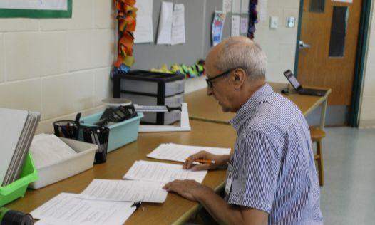 Caption:     A Passion for Physics: Physics teacher Mr. Eduardo Gil reviews students assignments at his desk during his planning period. Originally from Columbia, Mr. Gil studied civil engineering for six years before moving to the US to teach. Mr. Gil said, “[My favorite part is] how physics describes the motions of everything in the universe”. Photo by Ayaana Gupta