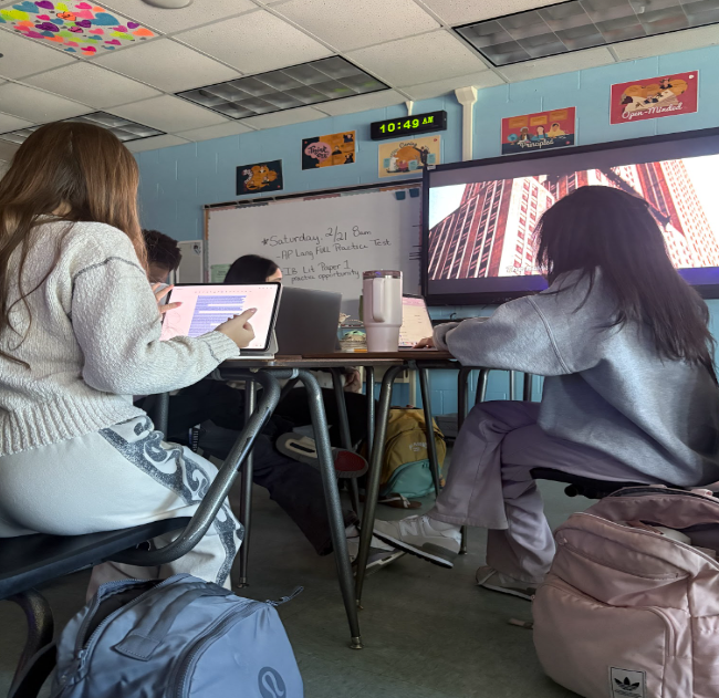 Caption: Preparing For The AP Exam: Belen Castillo and Lucie Frank study for the AP Language and Composition exam during class as they review essays and practice prompts. Castillo and Frank, both juniors, prepared for the full-length practice test earlier this semester to strengthen their understanding of pacing and question types. Before taking the three-hour simulation, they reviewed rhetorical strategies and practiced timed writing to improve their analysis skills. “It’s a lot to get done in a short amount of time,” Castillo said. Frank said the preparation helped her feel more confident, adding, “It’s meant to help us get used to the timing and format of the real exam.”