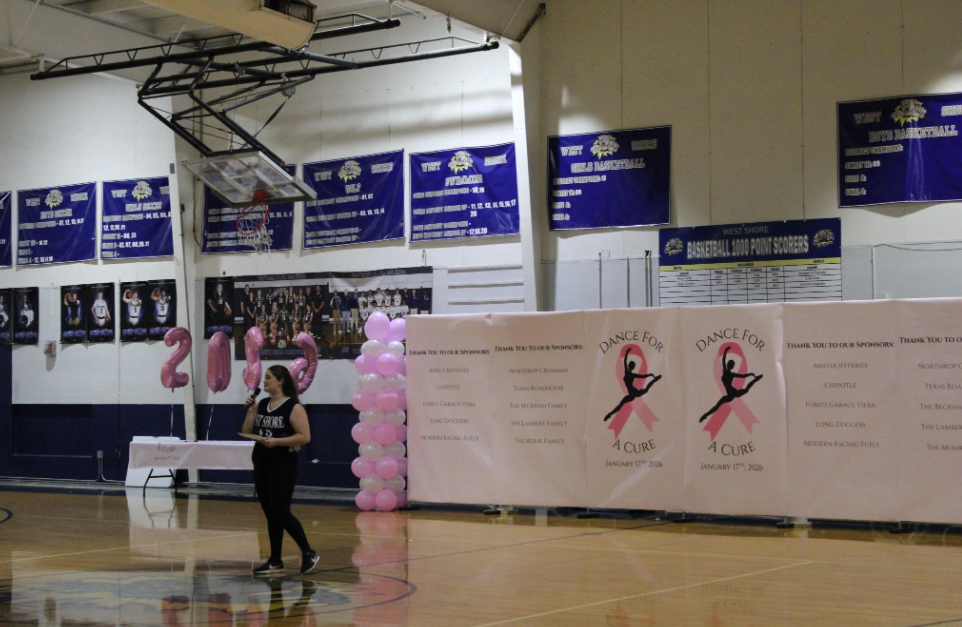 WHY WE ARE HERE: Senior Ava Hulbert steps up to speak at her “Dance For A Cure” event in the West Shore gym, a place where she had spent six years growing as a dancer within her 16‑year journey and had chosen to turn that passion into a senior project supporting local breast cancer charities. She had overcome unexpected venue setbacks — including being quoted nearly $4,000 elsewhere. She had relied on volunteers, teammates, family, and friends whose encouragement had carried her through every challenge. “I couldn’t have done any of this without the people who believed in me and stood by me every step of the way.”. Photo by Issy Perez