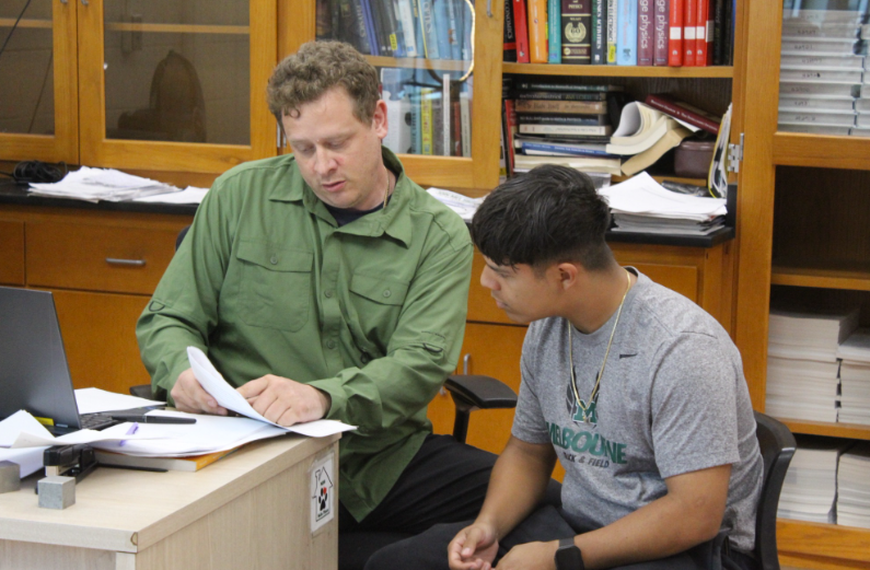 A Helping Hand: IB Physics teacher David Proctor shows senior Samuel Patarroyo where he can make improvements on his IB Physics Internal Assessment. After the students finished their rough drafts, Mr. Proctor met with them one on one to give them feedback before they had to turn in their final paper. “Mr. Proctor gave me great suggestions. For example, he suggested me to include a null hypothesis. He also explained how to format the IA,” said Patarroyo. Photo by Kyra Chang