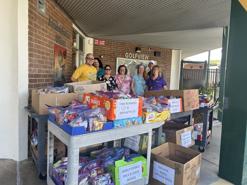 Photo of people standing in front of the school, behind carts full of food donations.