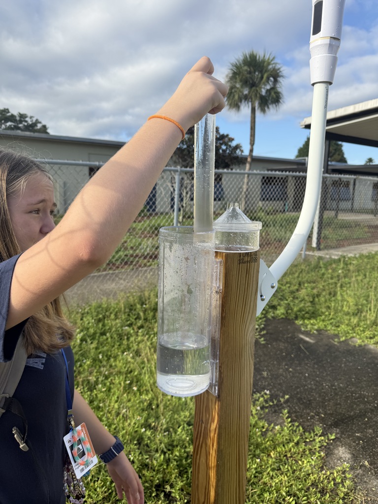 student pulling up rain gauge measurement tube full of water