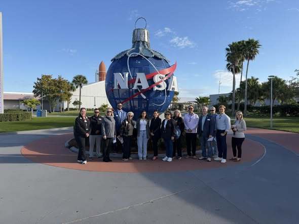 a group of teachers posing in front of the NASA sign at Kennedy Space Center during the 6th grade program