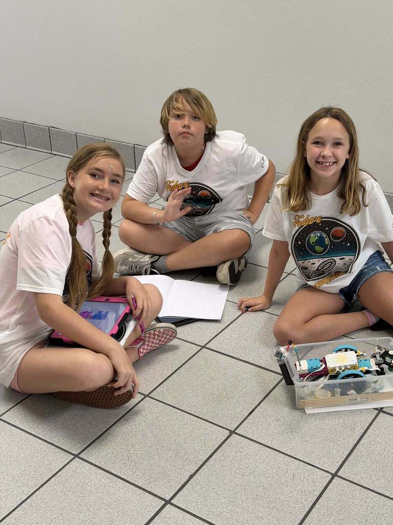 3 students sitting on the floor waiting for their turn to present