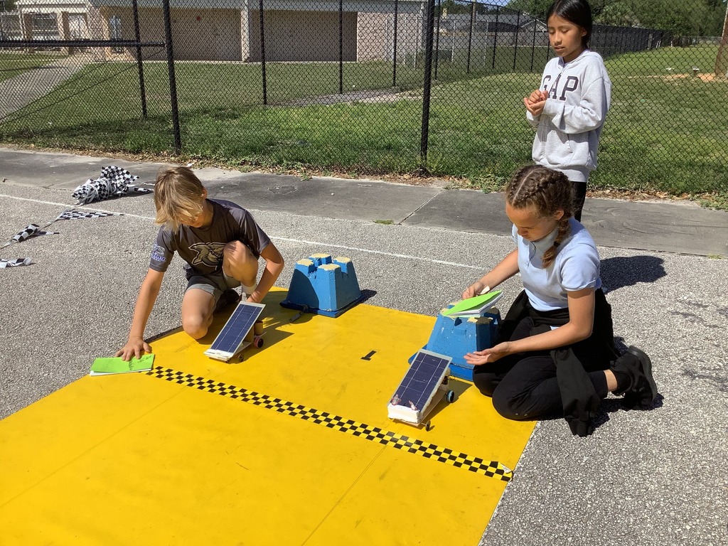 students outside using a yellow track to race their solar cars