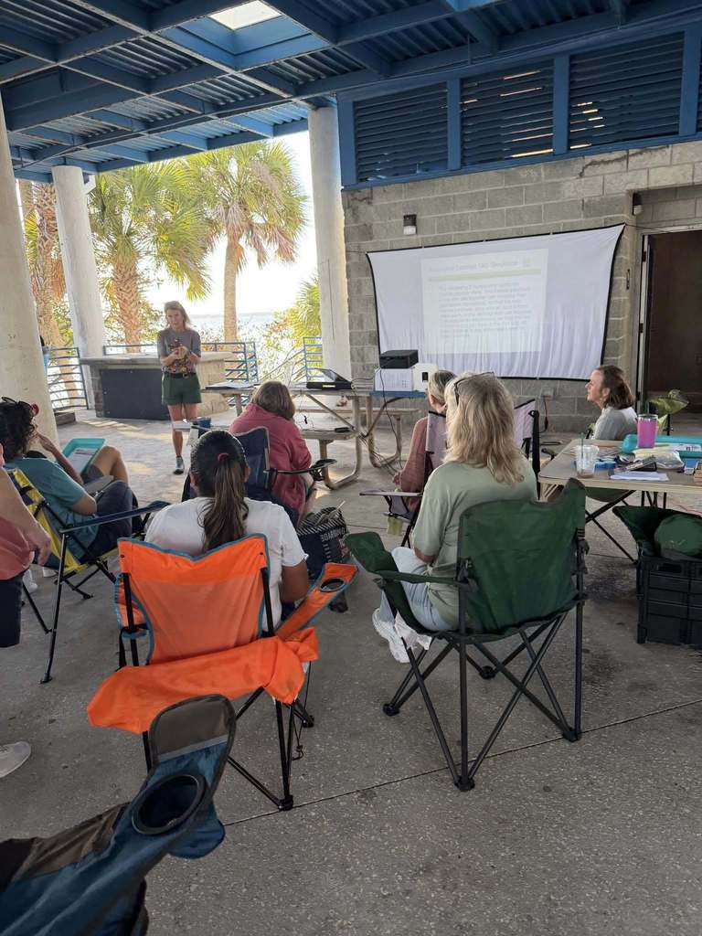 Participants listening to a lecturer and watching a presentation in an outdoor pavilion at the park