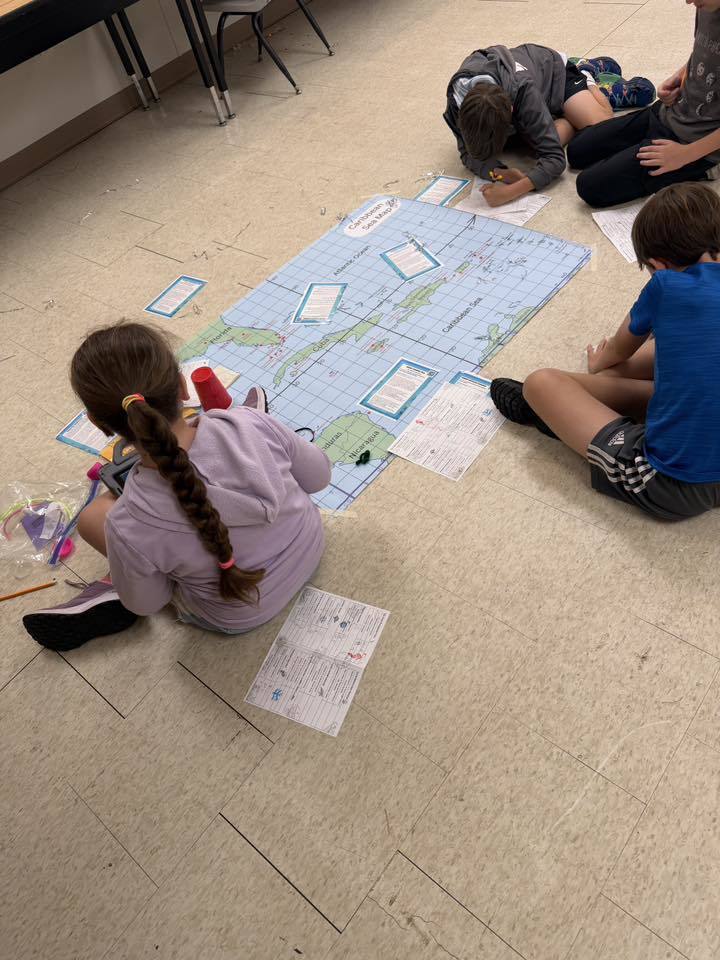 students sitting on the ground with a large map labeling it