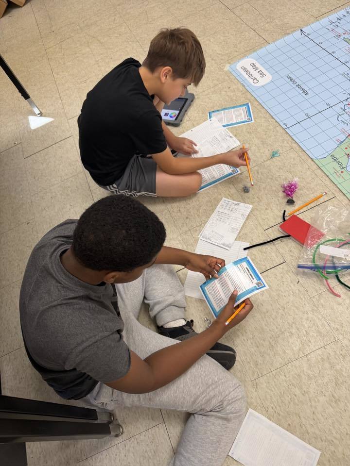 Students sitting on the floor working on a worksheet