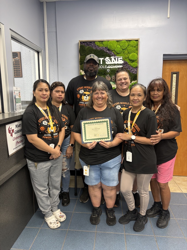 stone custodians standing in their school shirts holding a certificate in the front office