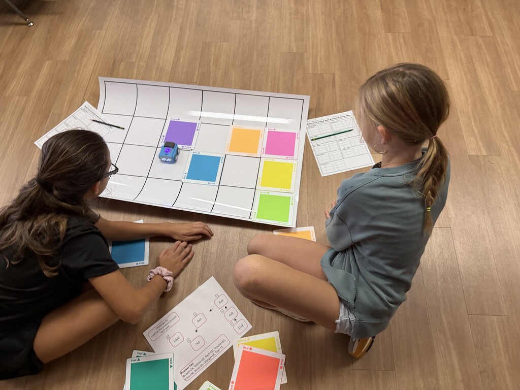 Two fourth-grade students sitting on the floor using colored coding tiles to guide Sphero indi robot.