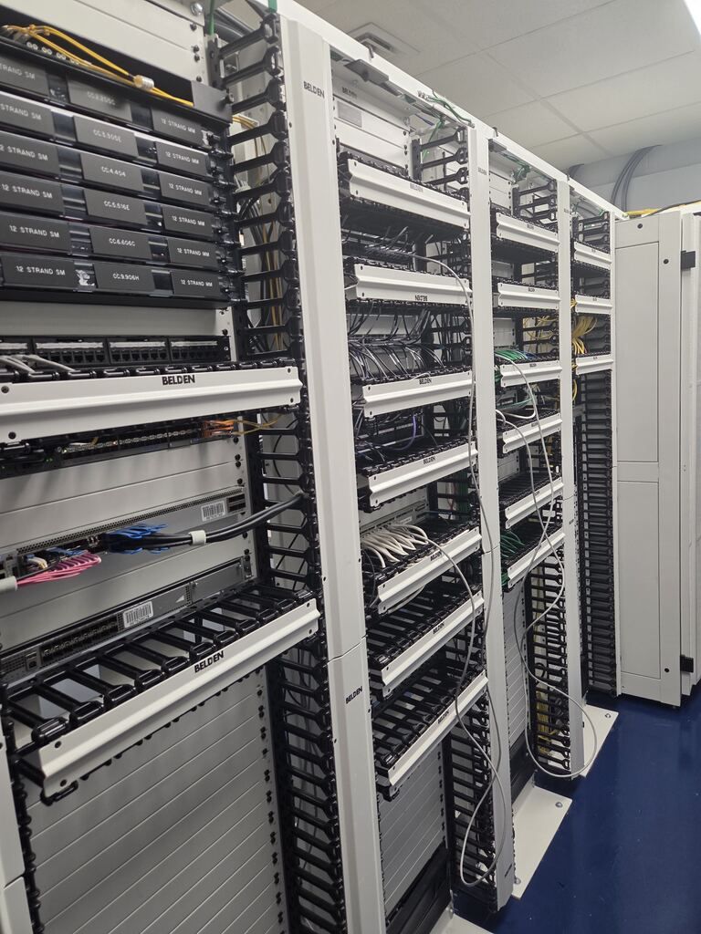 An overhead angled view of multiple rows of server racks and patch panels with organized cabling in a server room.