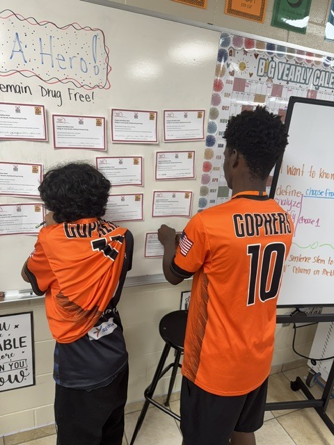 image of two stone students standing at a white board putting up pledge cards to stay drug free. 
