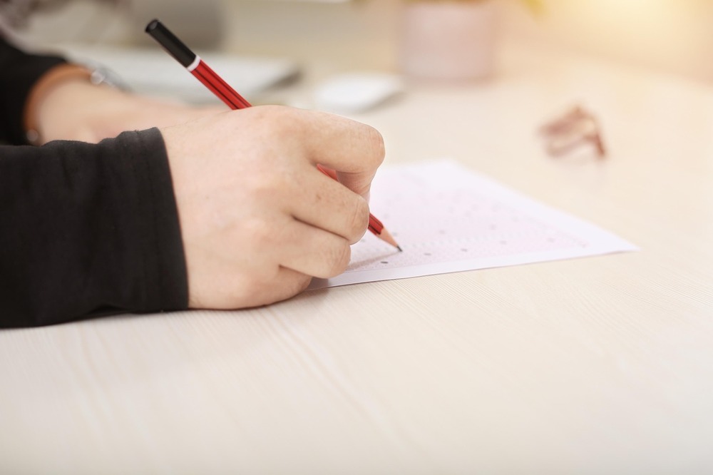 This photo is an up-close look at a student hand holding a pencil. The student is completing a test on top of a desk or table.