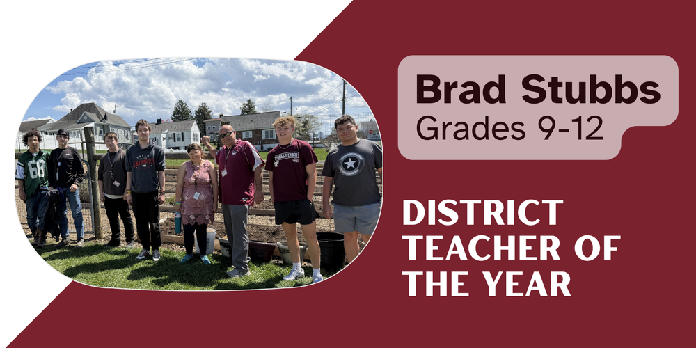 Brad Stubbs, District Teacher of the Year for grades 9–12, stands outdoors with a group of high school students in a school garden area. The group poses together on a sunny day with raised garden beds, houses, and a partly cloudy sky in the background.
