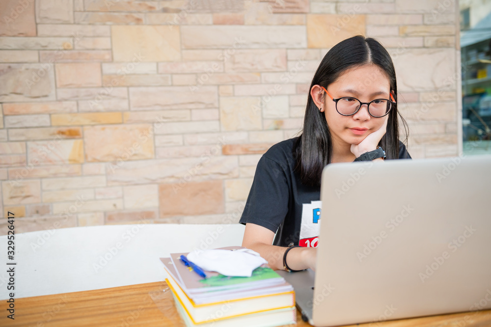 This image is of a middle school female student with glasses. The student has her laptop open and a stack of books next to the laptop.