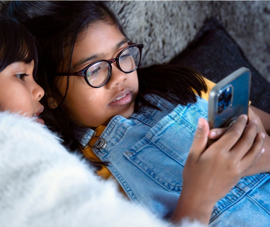 A middle school aged female is reclining on a sofa with a phone in her hand. She is looking at the phone screen.