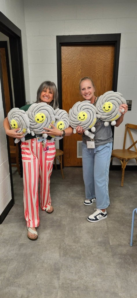 Two women smiling and holding several identical gray spiral plush toys with yellow smiling faces.