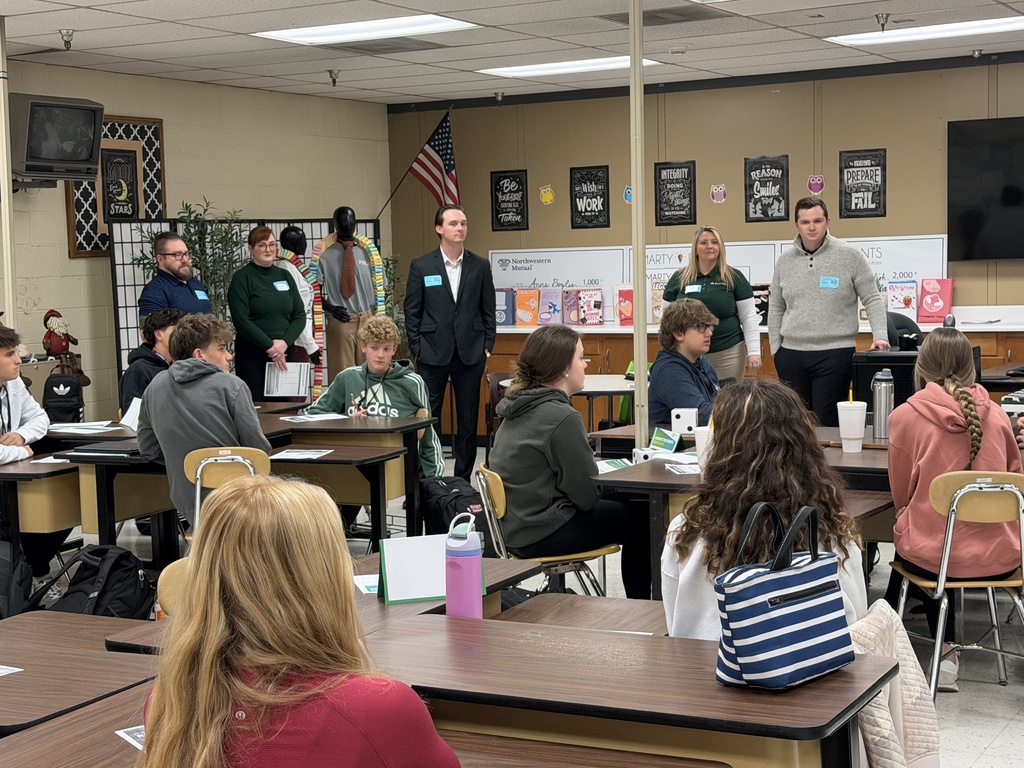 A group of high school students sits together reviewing their Reality Check worksheets, discussing transportation and food budget options at their table.