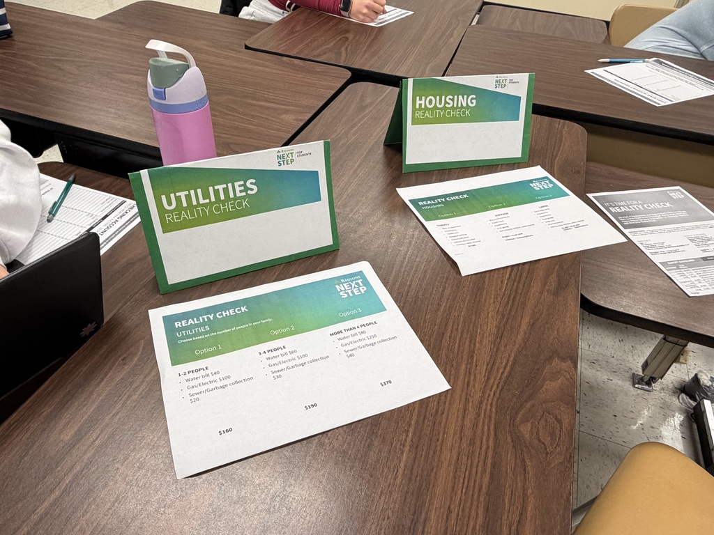 A Regions Bank representative holds up a checking account register and explains budgeting instructions to students during the Reality Check activity.