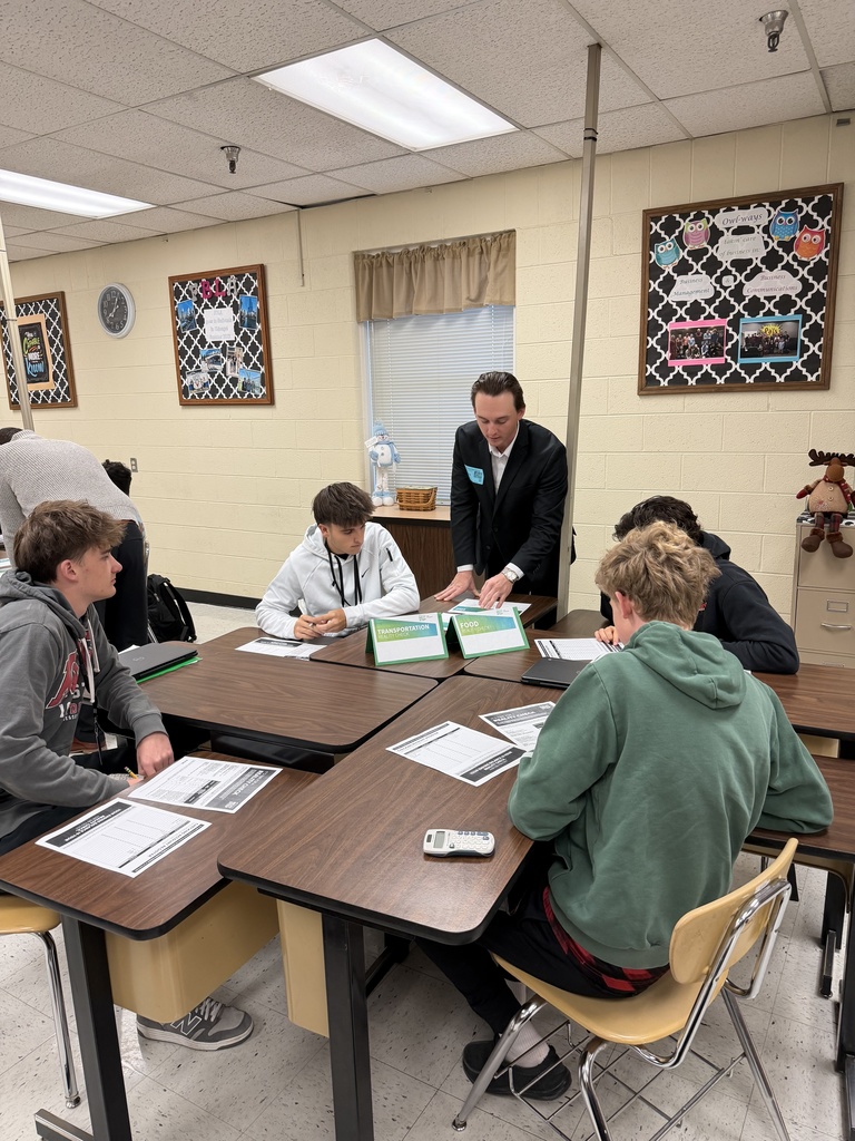 A Regions Bank volunteer meets with a student at the cell phone and subscriptions station, explaining monthly costs as part of the Reality Check activity.