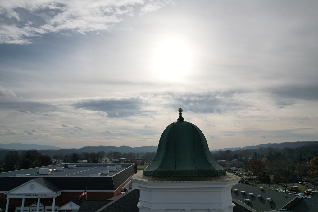 Aerial view of Tennessee High School’s green, domed cupola topped with a gold finial, rising above Viking Hall and the surrounding campus, with Bristol’s neighborhoods and rolling hills visible in the distance under a bright, cloud-filled sky.