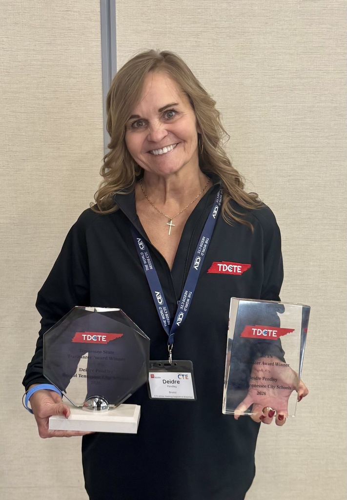 Deidre Pendley smiles while holding two glass TDCTE Trailblazer Award plaques—one for East Tennessee and one for the state of Tennessee—wearing a black TDCTE jacket and conference badge against a neutral background.