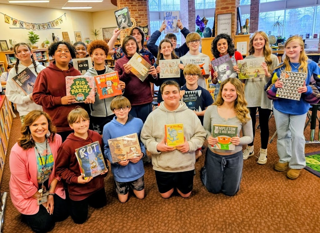 A group of Tennessee Middle School students and two teachers pose together in the Fairmount Elementary School library during Read Across America Week, each holding a favorite children’s book they shared with younger students during their visit.