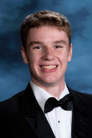Portrait of a smiling teenage boy wearing a black tuxedo jacket, white dress shirt, and black bow tie, posed against a blue studio background.