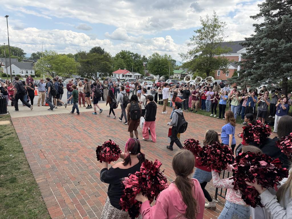 Students walk through a crowd of cheering supporters outside Tennessee High School as members of the Mighty Viking Band perform nearby. Cheerleaders with maroon pom-poms line the foreground while families, staff, and students gather along the walkway under a cloudy afternoon sky.