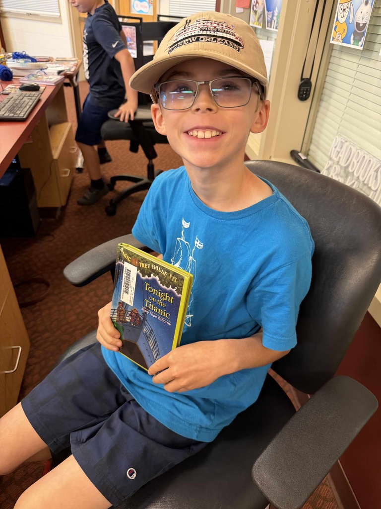 A smiling student proudly holds Tonight on the Titanic from the Magic Tree House series after choosing it for Drop Everything and Read (DEAR) time in the Fairmount Elementary School library.