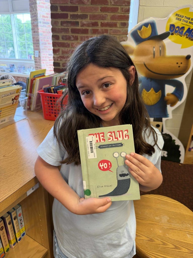 A smiling student holds up The Slug by Elise Gravel after selecting it during Drop Everything and Read (DEAR) time in the Fairmount Elementary School library.