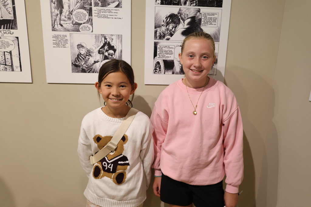 Two Holston View Elementary fifth-grade students, Ayana and Caroline, smile for a photo in front of black-and-white illustrations during a visit to the Birthplace of Country Music Museum.