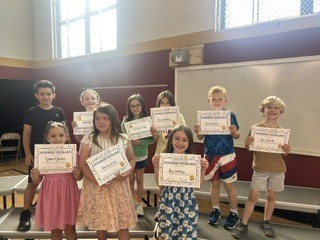 Ten students pose in two rows in a school gymnasium, each holding a certificate.