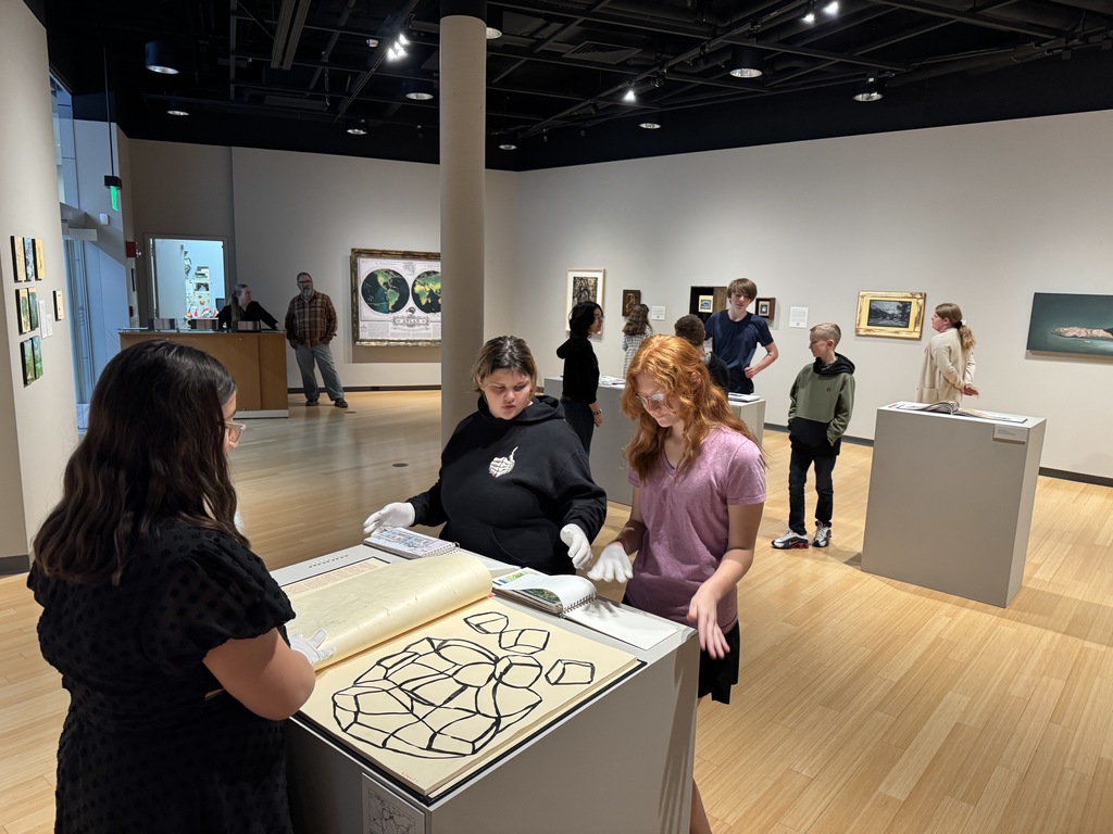 Students wear white gloves while viewing a large handmade artist book.