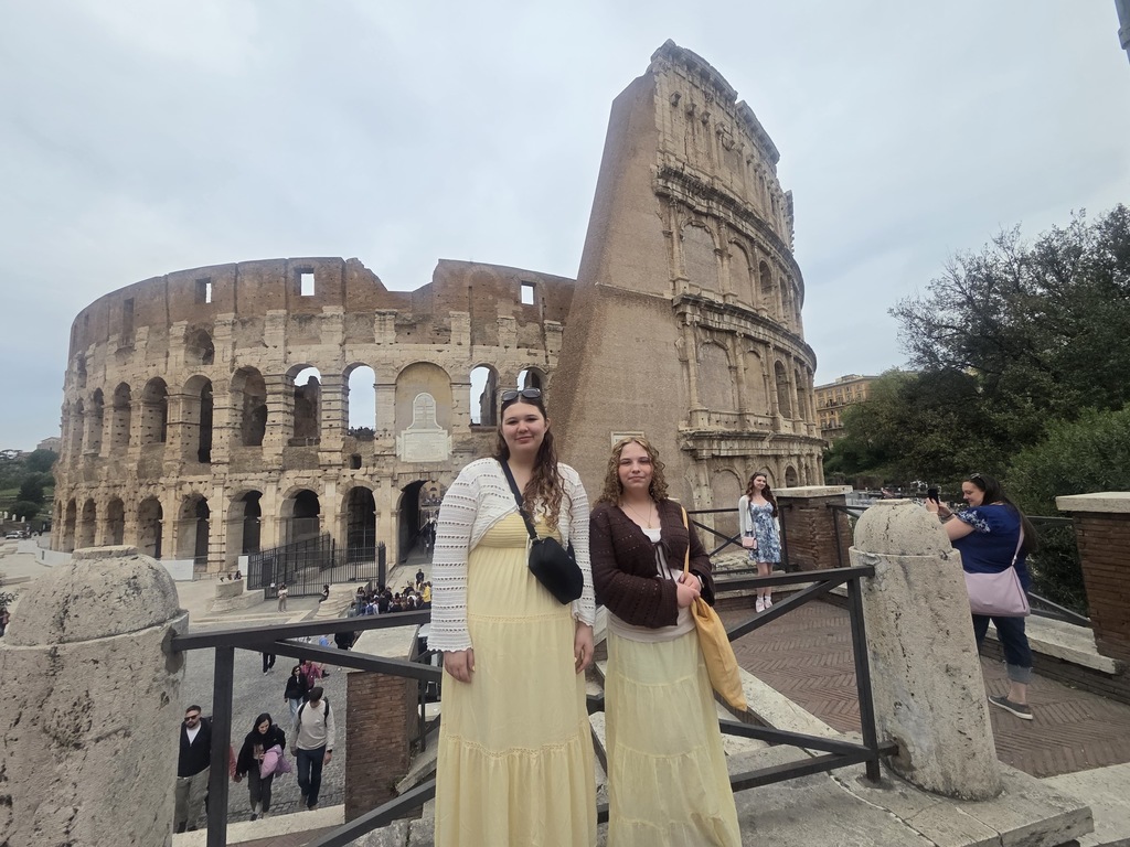 Two students, in dresses, standing in front of the Colosseum, on a nice spring day
