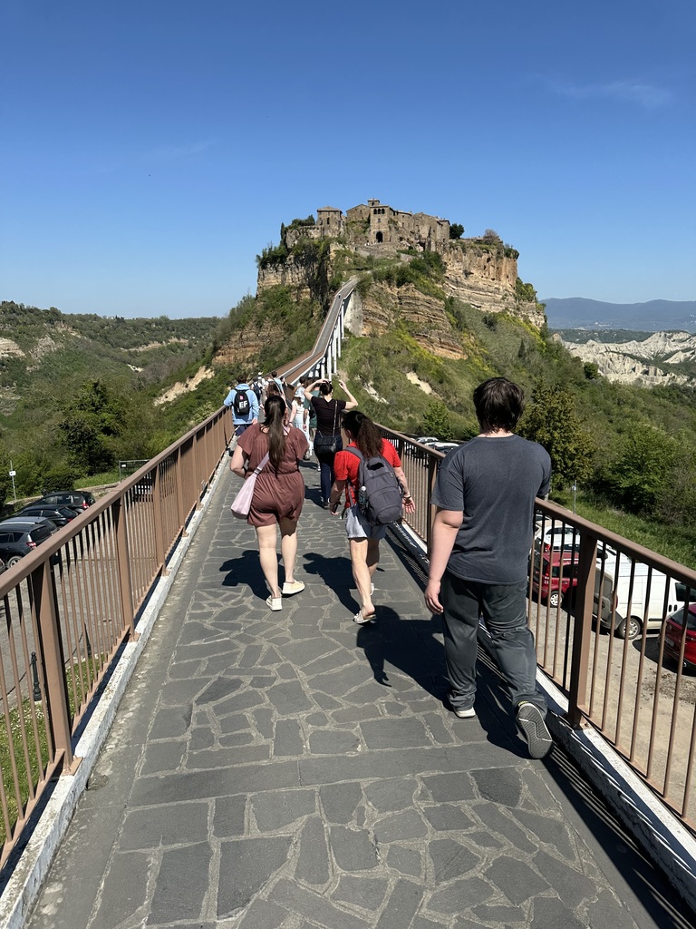 Students staff and parents walk on a narrow walkway toward Civita di Bagnoregio, a dying medieval city on a hilltop