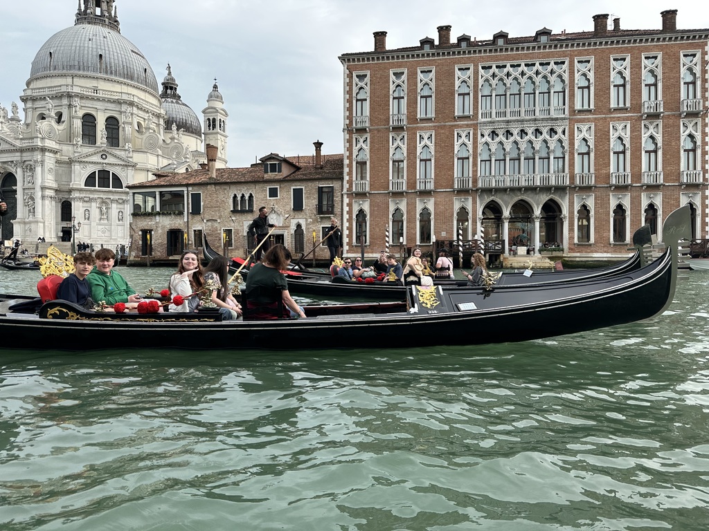 Students staff and parents in gondola boats on the canals of Venice, with buildings in the background