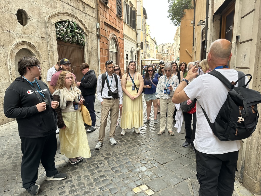 Students, staff, and parents listen to a local tour guide on a food tour through Rome