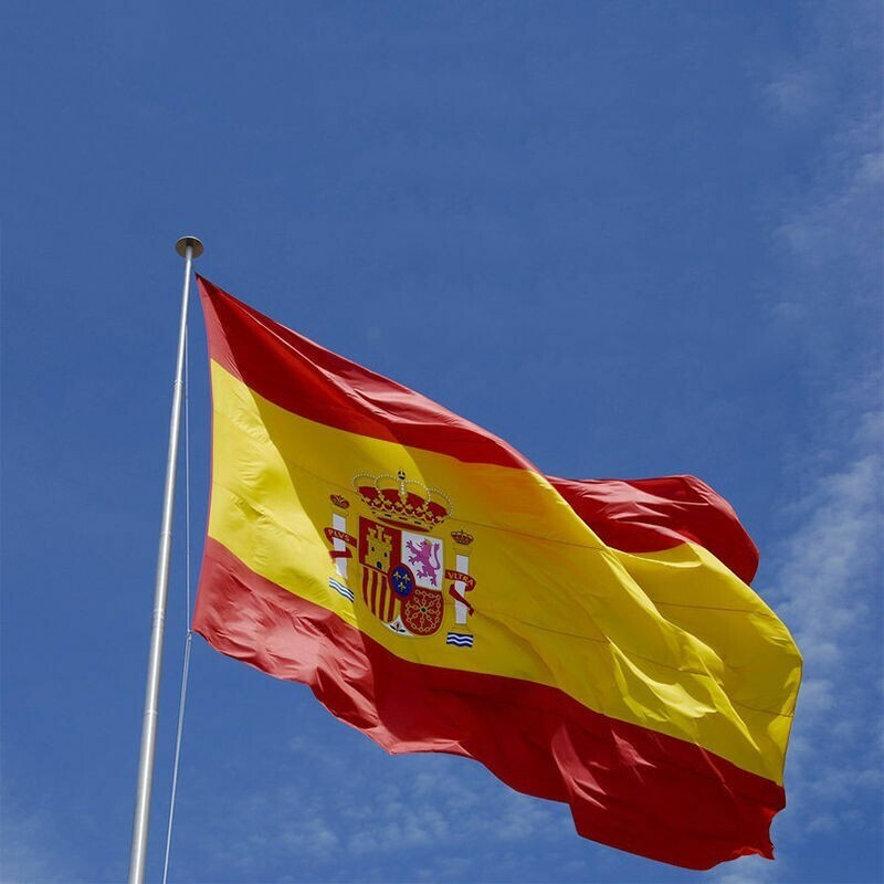 Red and yellow Spanish flag blowing in the wind before a blue sky 