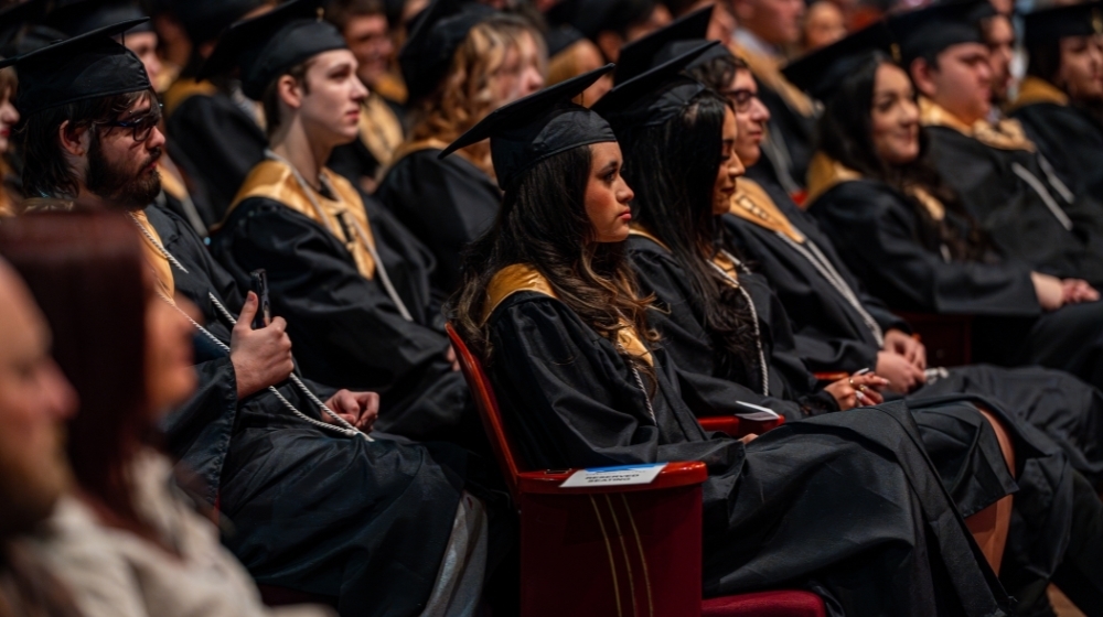 Graduating students in black caps and gowns seated during a commencement ceremony.