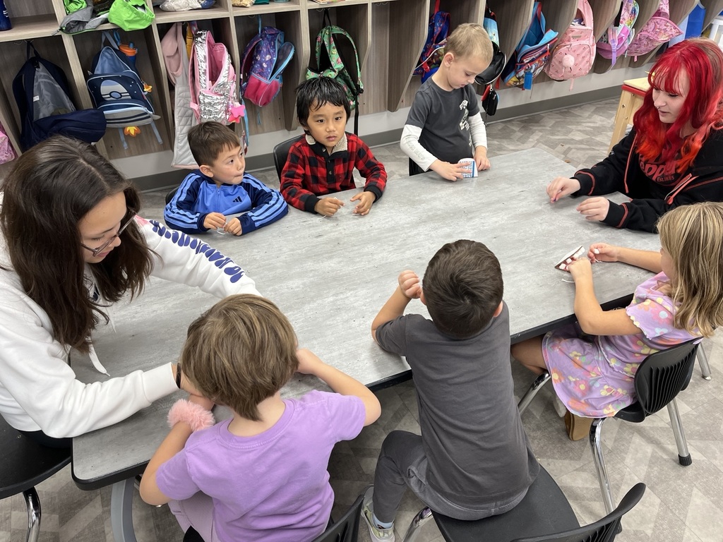 Preschool students around a table while an older student leads a dental health lesson.