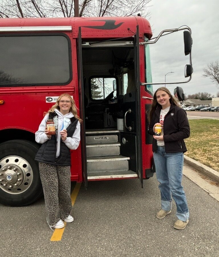 Tyanna and Natalee in front of the bus holding jars of sauce. 