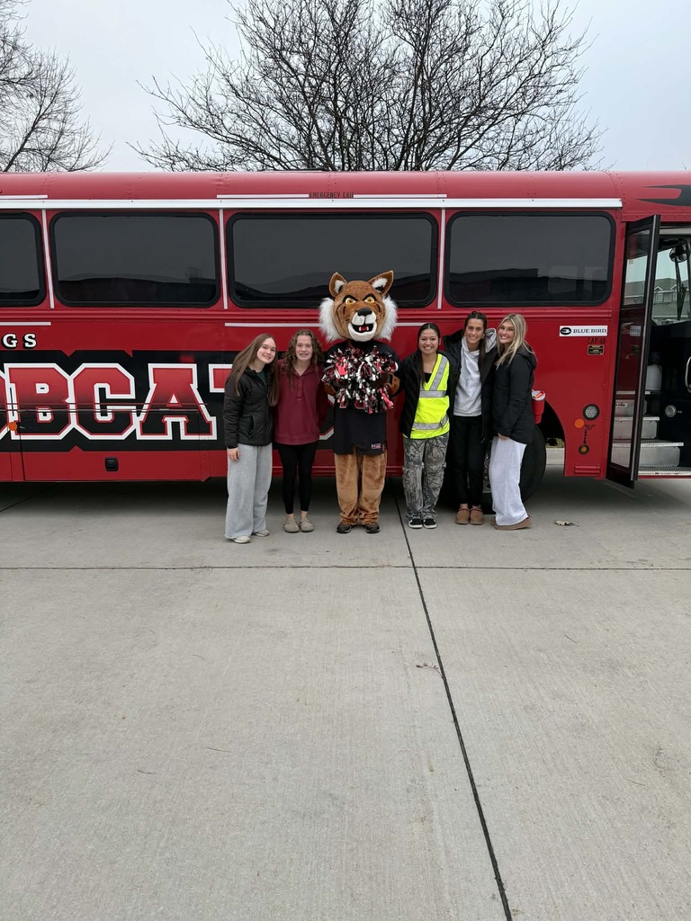 Bobby the bobcat standing in front of the bus with five high school students.