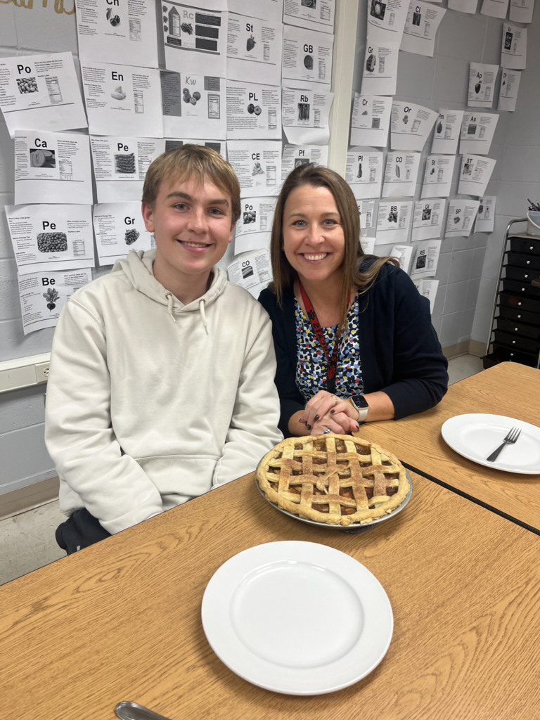 A student with a guest showing off their apple pie.