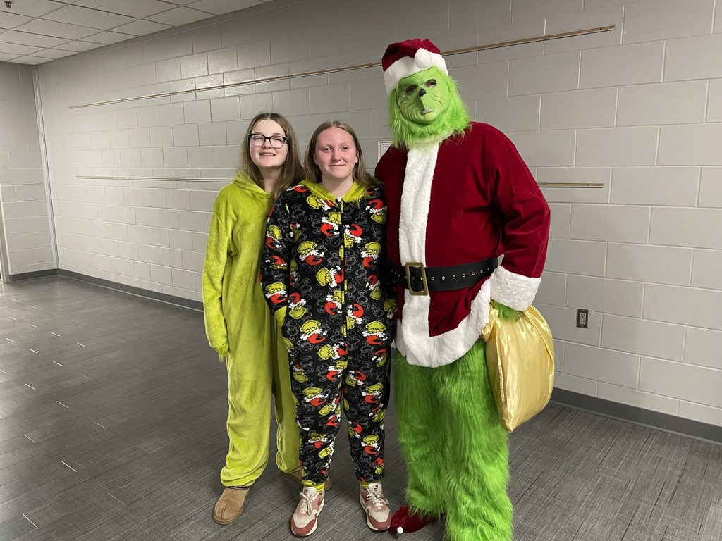 Two students dressed up in Grinch onesies posing with a staff member dressed up as The Grinch.