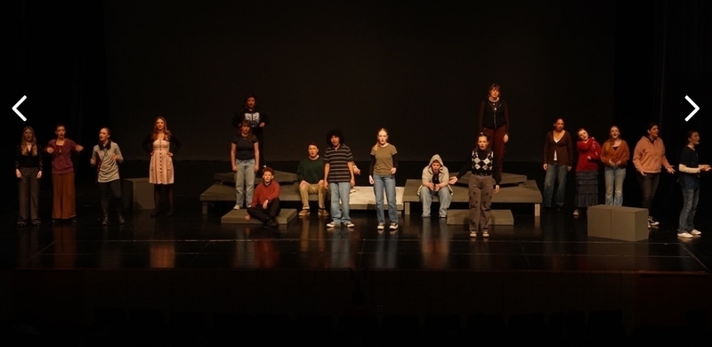 Students performing on stage. A large group stretched out across the whole stage.